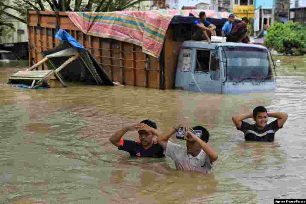 People wade past an inundated lorry stuck in floodwaters in Lhoksukon, North Aceh, Indonesia, following heavy rainfall in the region.