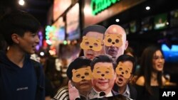 Mwanamke amevaa nyuso za bandia kadhaa za Kiongozi wa Hong Kong Carrie Lam (kushoto chini) na Rais wa China Xi Jinping (katikati chini) wakiandamana wakati wa sikukuu ya Halloween, Hong Kong, Octoba 31, 2019.