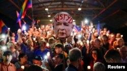 Para pengunjuk rasa mengacungkan poster yang bertuliskan “Memalukan” dan menggambarkan wajah pemimpin Partai Hukum dan Keadilan (PiS) Jaroslaw Kaczynski, dalam unjuk rasa menentang reformasi peradilan di Krakow, Polandia, 16 Juli 2018.

