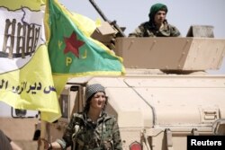 FILE - A female fighter from the Syrian Democratic Forces stands near a military tank in the village of Abu Fas, Hasaka province, Syria, Sept. 9, 2017.