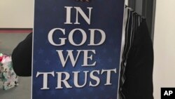 FILE - Wyoming state Rep. Cheri Steinmetz, R-Lingle (not seen), on Tuesday, March 6, 2018, shows an example of an "In God We Trust" placard in Cheyenne, Wyo. Steinmetz is sponsoring a bill that would allow people to donate such placards for display in prominent plac
