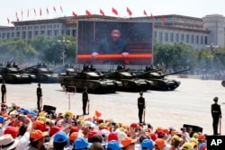 In this Thursday, Sept. 3, 2015 file photo, Chinese President Xi Jinping is displayed on a big screen as Type 99A2 Chinese battle tanks roll across during a parade.