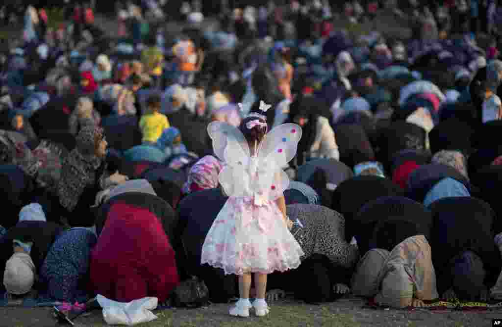 Seorang anak perempuan mengenakan pakaian dengan model kupu-kupu berdiri di depan jamaah perempuan yang melakukan shalat Idul Fitri di kota Gaza, Palestina.