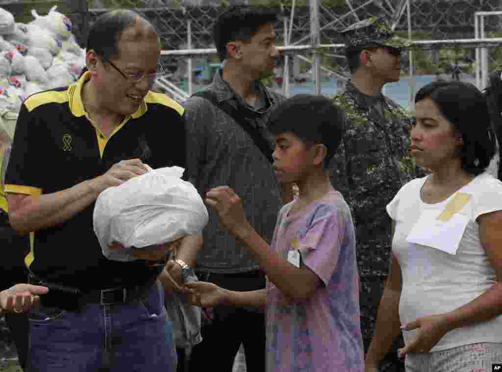 Philippine President Benigno Aquino, left, helps to distribute relief goods to victims of Typhoon Bopha during his visit to New Bataan township, Compostela Valley, Philippines, December 7, 2012.