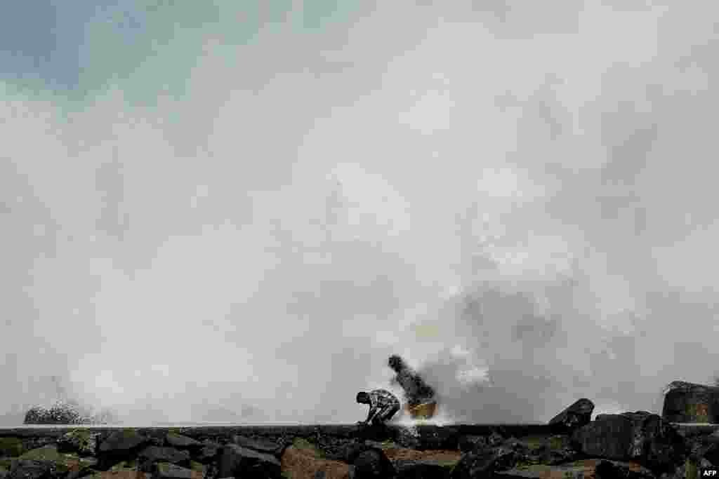 Men walk past as waves hit a breakwater at Kasimedu fishing harbor in Chennai, May 19, 2020, as Cyclone Amphan barrels toward India&#39;s eastern coast.