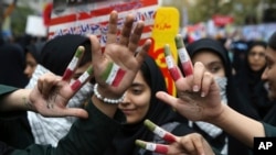 Iranian schoolgirls hold up their hands painted with the colors of their country's flag and writing in Persian that reads "Death to America," in an annual gathering in front of the former U.S. Embassy marking the anniversary of its 1979 takeover, in Tehran, Iran, Nov. 4, 2017.