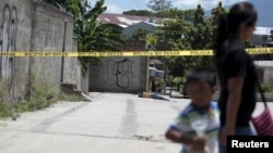 A woman and a child walk past a crime scene where the body of a dead man was found after he was shot by alleged gang members in the El Castillo neighborhood in Soyapango, on the outskirts of San Salvador, El Salvador, July 20, 2015.