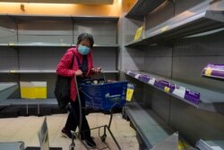 Una mujer usando una máscara pasa frente a estantes vacíos en un supermercado en Hong Kong, el jueves, 6 de febrero de 2020.