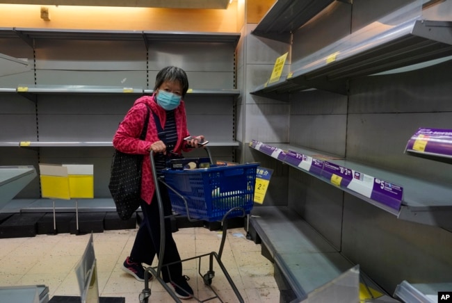 Una mujer usando una máscara pasa frente a estantes vacíos en un supermercado en Hong Kong, el jueves, 6 de febrero de 2020.