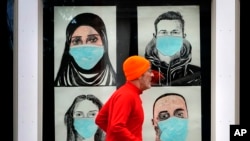 n this Nov. 16, 2020, file photo, a runner passes by a window displaying portraits of people wearing face coverings to help prevent the spread of the coronavirus in Lewiston, Maine. A deadly rise in COVID-19 infections is forcing state and local officials to adjust their blueprin