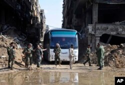 FILE - In this file photo released April 30, 2018 by the Syrian official news agency, SANA, Syrian government forces oversee a bus carrying al-Qaida-linked fighters during an evacuation from the Palestinian refugee camp of Yarmouk, near Damascus, Syria.
