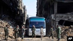 FILE - In this file photo released April 30, 2018 by the Syrian official news agency, SANA, Syrian government forces oversee a bus carrying al-Qaida-linked fighters during an evacuation from the Palestinian refugee camp of Yarmouk, near Damascus, Syria.