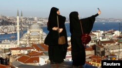 Young women take selfie photographs in front of the New Mosque by the Bosphorus strait in Istanbul, Turkey, Jan. 12, 2016. A Syrian suicide bomber is thought to be responsible for an attack which killed at least ten people including foreigners in the hear