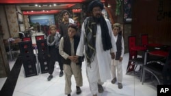 In this photo taken July 25, 2017, Mohammed Naseer, with black turban, holds his sons' hand when they enter a Pizza Restaurant in Kabul, Afghanistan. Mohammed Naseer spent several weeks arranging for his son, a nephew and several other children from his d