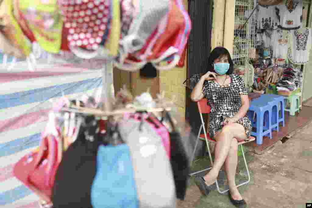 کسادی بازار در ویتنام. صاحب این فروشگاه با زدن ماسک، بیرون از مغازه&zwnj;اش در هانوی ویتنام به انتظار مشتری نشسته است.