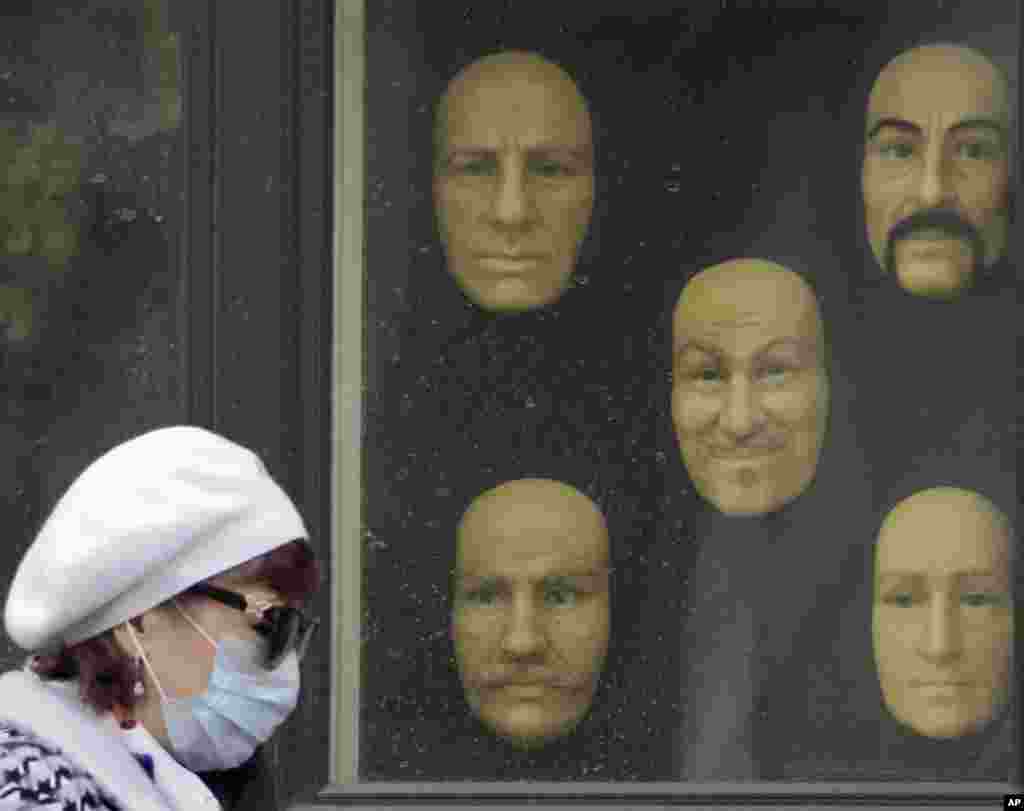 A woman wearing a face mask walks past wax faces displayed in a window of a wax museum in St.Petersburg, Russia, May 4, 2020.