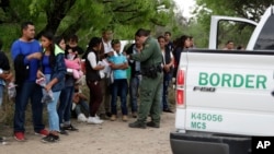 FILE - A U.S. Border Patrol agent checks the names and documents of families who crossed the nearby U.S.-Mexico border, near McAllen, Texas, March 14, 2019. 