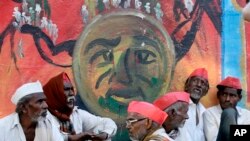 Indian farmers sit in front of a graffiti at the end of their six day long march on foot, in Mumbai, India, Monday, March 12, 2018.