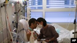 Pasangan Amelie dan Ludo Khayat saling berpegangan di dalam ruangan perawatan khusus pasien COVID-19 di Rumah Sakit Timone, Marseille, Prancis, pada 23 Desember 2021. Ludo, 41, beranjak pulih setelah mengalami koma selama 24 hari akibat infeksi COVID-19. (Foto: AP/Daniel Cole)