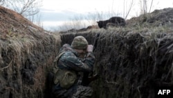 FILE - A cat looks down at a Ukrainian soldier resting in a trench on the front line with Russia backed separatists near Krasnogorivka village, Donetsk region, Feb. 28, 2020.
