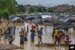 FILE - Rohingya Muslims, who crossed over from Myanmar into Bangladesh, carry their children and belongings after their camp was inundated with rainwater near Balukhali refugee camp, Bangladesh, Sept. 19, 2017.