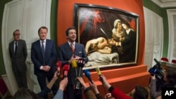 Auction officer Marc Labarbe, center left, and Eric Turquin expert specialized in old master paintings stand next to a 400-year-old painting that might have been executed by Italian master Caravaggio and could be worth more than 100 million euros, found in an attic in Southern France, and presented in Paris, April 12, 2016.