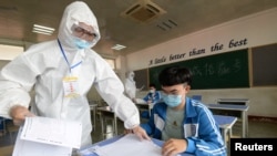 An invigilator in protective suit distributes test papers to students at an isolation site during a mock examination ahead of the annual national college entrance exam, or "gaokao", which has been postponed by one month due to the coronavirus disease (COVID-19) outbreak