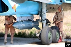 In this photo taken on Saturday, Oct. 3, 2015, Russian military support crew attach a satellite guided bomb to SU-34 jet fighter at Hmeimim airbase in Syria.