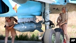 In this photo taken on Saturday, Oct. 3, 2015, Russian military support crew attach a satellite guided bomb to SU-34 jet fighter at Hmeimim airbase in Syria. 