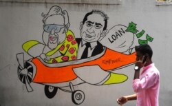 Seora ng pejalan kaki berjalan melewati dinding bergambar grafiti kartun pengusaha India Vijay Mallya (kiri) dan Nirav Modi (kanan) yang dicari oleh Interpol, 2 April 2019. (Foto: dok).