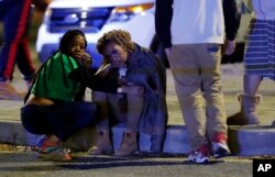 Two women watch as police investigate the scene of a Mardi Gras day shooting in New Orleans, Feb. 13, 2018.