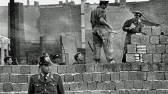 圖為1961年10月7日一名西柏林士兵站立在分割東、西柏林的混凝土牆邊。 他身後為東柏林工人正在加高圍牆