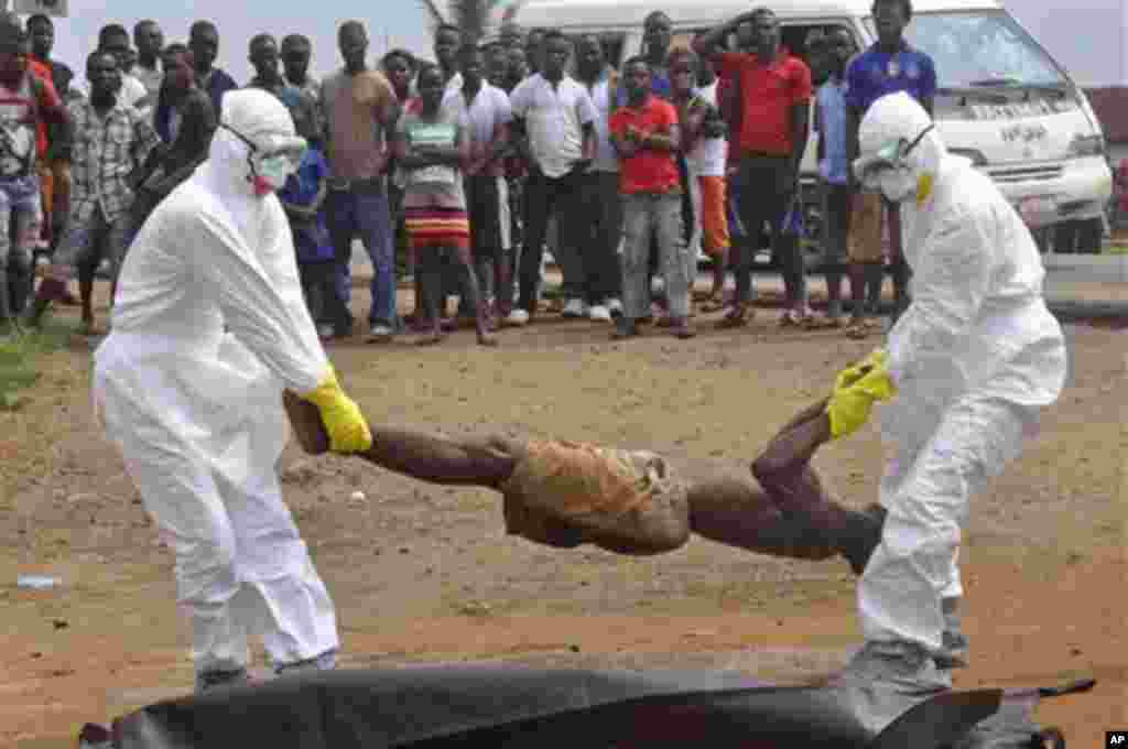 Health workers places the body of a man, inside a plastic body bag as he is suspected of dying due to the Ebola virus as people, rear, look on in Monrovia, Liberia, Thursday, Sept. 4, 2014. (AP Photo/Abbas Dulleh)