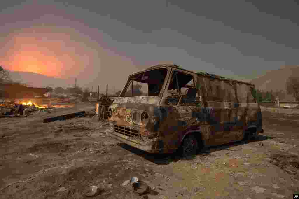 Seen in a long exposure nighttime photograph, a burned van rests in a lot while a wildfire glows on the horizon in Phelan, California, Aug. 18, 2016.