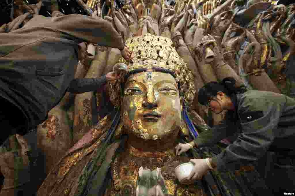 Restoration workers peel off loose gold foil as part of a restoration project for an 800-year-old Thousand-Hand Guanyin Buddhist statue on Mount Baoding in Chongqing municipality, China. The stone statue, which takes up about 88 square meters on the mountain, dates back to the Southern Song Dynasty (1127-1279).