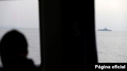 FILE - A Greek coast guard officer watches a NATO warship during a patrol on the Aegean Sea, March 17, 2017. A year later, a search and rescue operation is trying to locate about a dozen migrants whose boat reportedly sank.