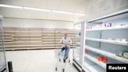 FILE: A customer pushes her trolley next to empty shelves at a Sainsbury's store during the COVID-19 outbreak, in Harpenden, Britain, March 18, 2020.