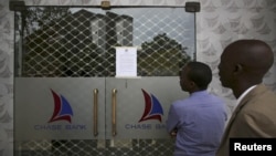 People read a notice from the Central Bank of Kenya taped to the closed entrance of a Chase Bank branch, after the bank was put under receivership, in Nairobi, April 8, 2016. 