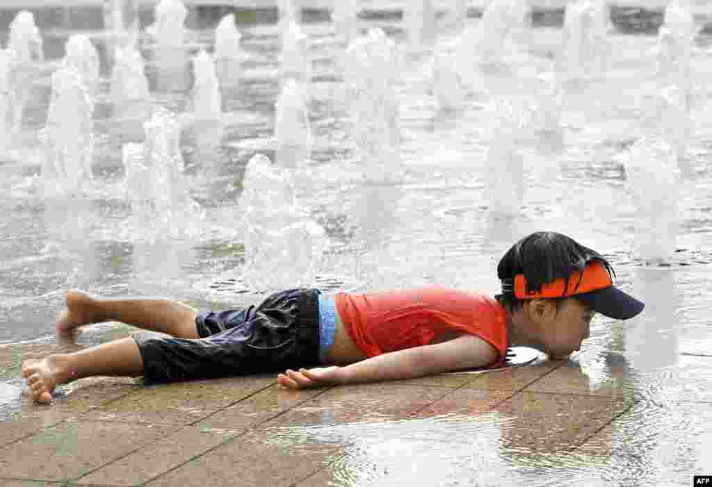 Một cậu bé Hàn Quốc nằm cạnh một đài phun nước ở trung tâm Seoul để giải nhiệt.