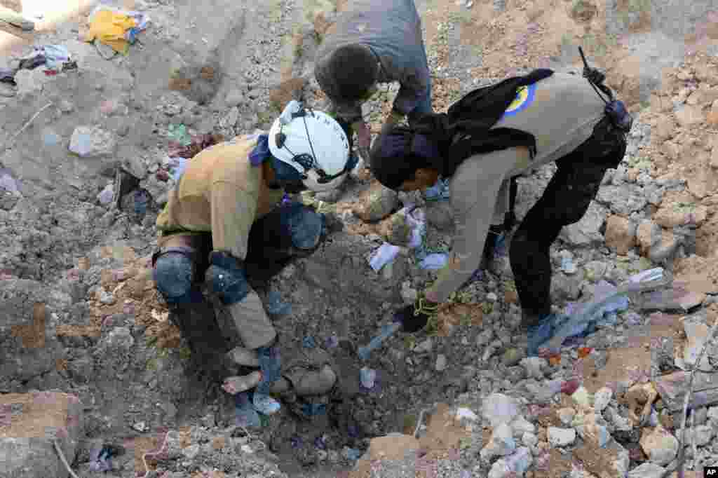 In this photo provided by the Syrian Civil Defense group known as the White Helmets, shows members of Civil Defense removing a dead body from under the rubble after airstrikes hit in Aleppo, Sept. 24, 2016. 