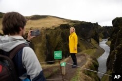 In this photo taken Wednesday, May 1, 2019, Russian tourist Nadia Kazachenok poses for a photograph taken by Mikhail Samarin at the Fjadrárgljúfur.