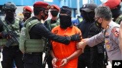 FILE - Police escort suspected militant Zulkarnaen, center, who is also known as Aris Sumarsono, upon arrival at Soekarno-Hatta International Airport in Tangerang, Indonesia, Dec. 16, 2020. 