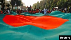 Orang-orang mengibarkan bendera besar Bangladesh, tiga hari menjelang peringatan 50 tahun Hari Kemenangan negara itu, di depan gedung parlemen di Dhaka, Bangladesh, 13 Desember 2021. (Foto: REUTERS/Mohammad Ponir Hossain...