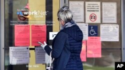 A woman checks job application information in front of IDES(Illinois Department of Employment Security)/WorkNet center in Arlington Heights, Ill., Thursday, April 9, 2020.