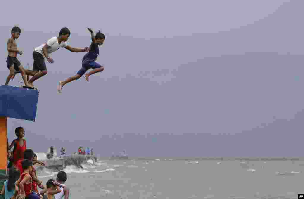 Boys jump into the water despite strong waves after a strong downpour at Manila&#39;s bay, Philippines.