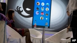 FILE - A woman sits near a display showing the dangers of hackers breaking into mobile devices during the Global Mobile Internet Conference in Beijing, China, April 29, 2016.