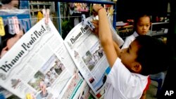 Seorang anak laki-laki menggantungkan koran berbahasa Inggris Phnom Penh Post di sebuah kios koran di Phnom Penh, Kamboja. (Foto: Dok)