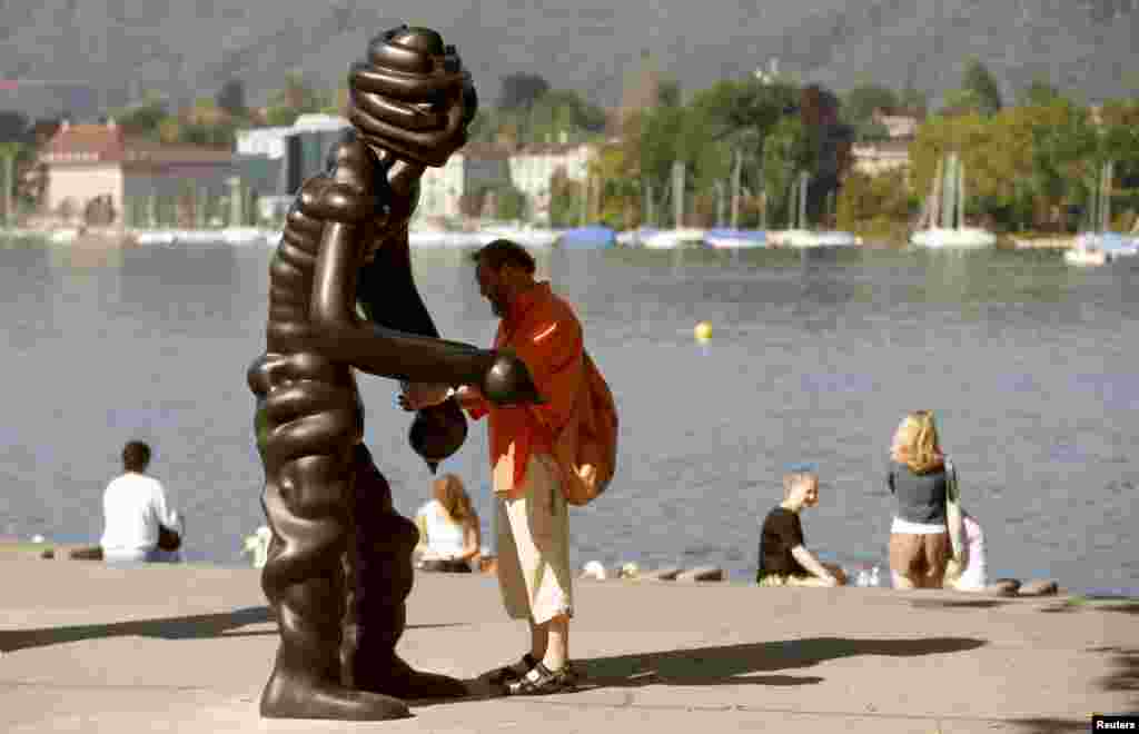 A man stands beside a sculpture of the group 'Vier Grosse Geister' (Four Big Ghosts') from 2003 by German artist Thomas Schuette on the borders of Lake Zurich in Zurich, Switzerland.