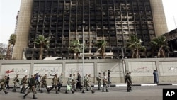 FILE - Army soldiers march in front of the burned-out headquarters of the National Democratic Party in Cairo, Feb. 15, 2011.
