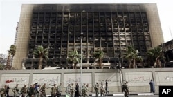 Army soldiers march in front of the burned down building of former President Hosni Mubarak's National Democratic Party in Cairo, Egypt, February 15, 2011